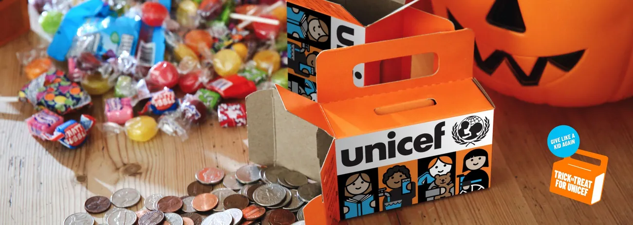 An orange Trick-or-Treat for UNICEF box beside a pile of Halloween candy, coins and a jack-o’-lantern